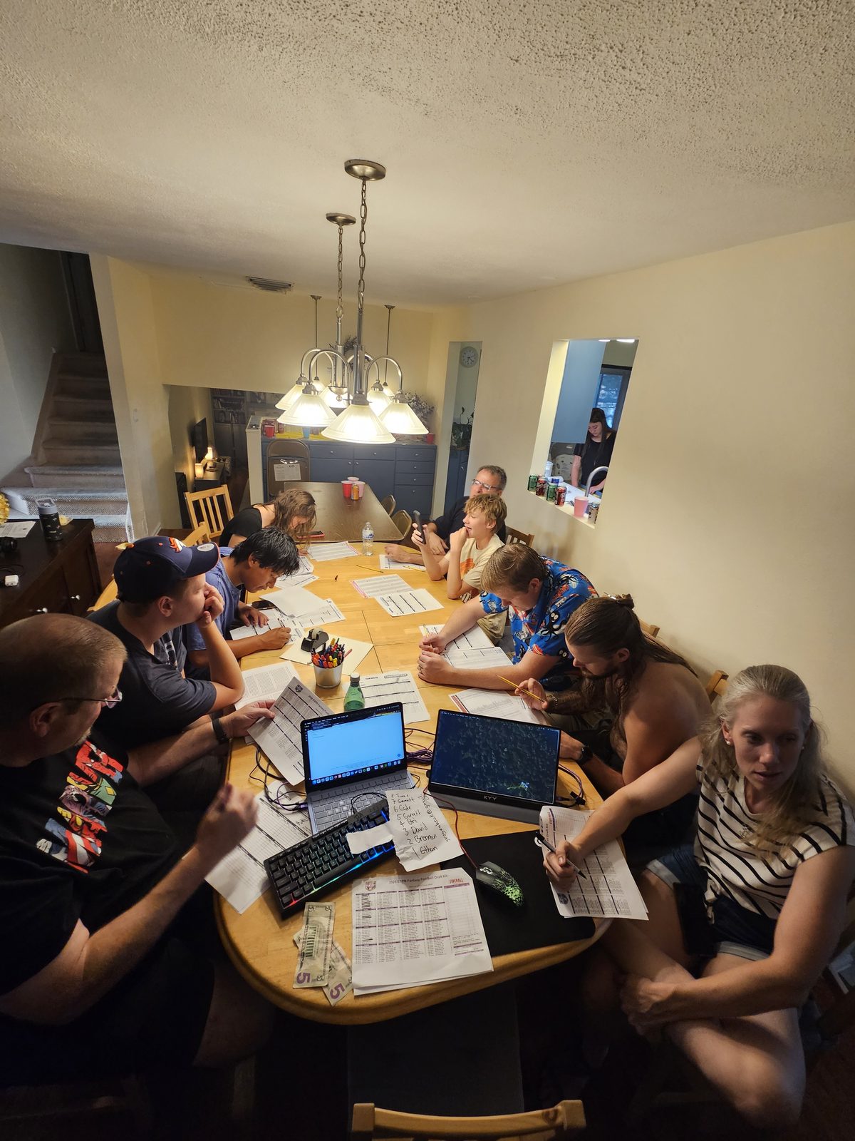 The whole group seated around the dining table for the draft, laptops and printed sheets spread out, buy-in cash on the table